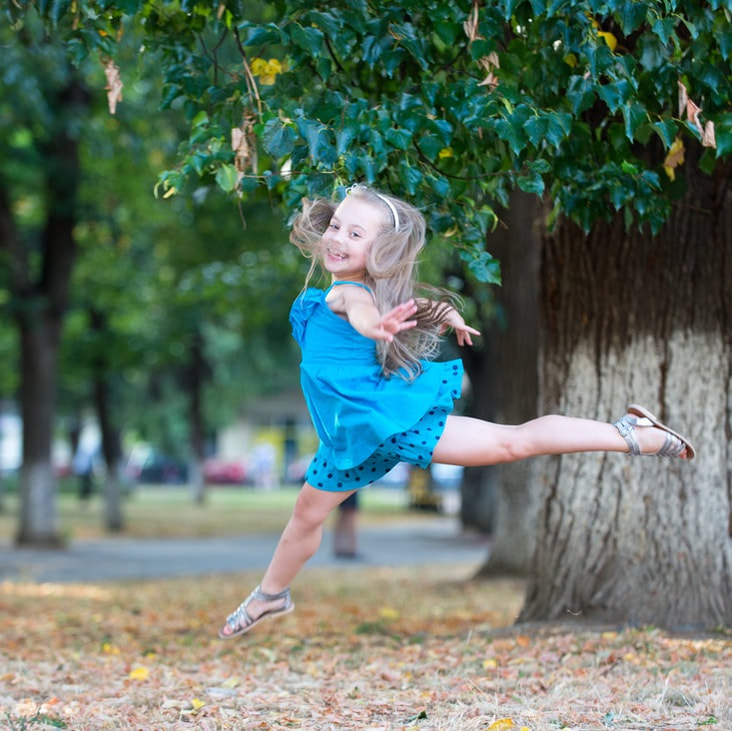 Child gleefully leaping outdoors under trees.