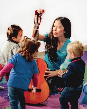 Music Together teacher shows guitar to group of children.