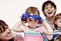Child wears tambourine as hat, playing with her two moms and brother.