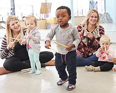 Music Together Mixed Age Class Child plays rhythm sticks with grownups and classmates.
